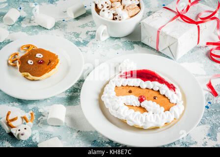 Idee für Kinder Weihnachten Frühstück: Pfannkuchen wie Santa Claus und Rotwild eingerichtet, Kakao mit Teddybären und Rotwild Marshmallow. Auf einem Hellblau Stockfoto