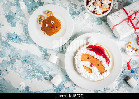 Idee für Kinder Weihnachten Frühstück: Pfannkuchen wie Santa Claus und Rotwild eingerichtet, Kakao mit Teddybären und Rotwild Marshmallow. Auf einem Hellblau Stockfoto