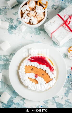 Idee für Kinder Weihnachten Frühstück: Pfannkuchen eingerichtet wie Santa Claus, Kakao mit Teddybären und Rotwild Marshmallow. Auf einem hellblauen backgroun Stockfoto