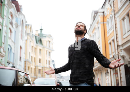 Porträt eines zufriedenen bärtigen Mann in Pullover stehen mit ausgestreckten Händen und sah auf einer Straße der Stadt Stockfoto