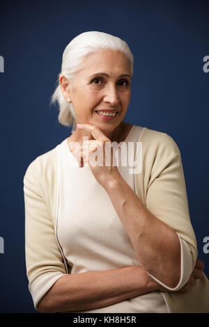 Foto von charmanten reife Frau in Beige t-shirt, ihr Kinn Holding, Kamera, auf dunkelblauem Hintergrund Stockfoto