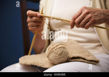 Zugeschnittenes Bild der alten Frau sitzt auf dunkelblauem Hintergrund beim Stricken. Stockfoto