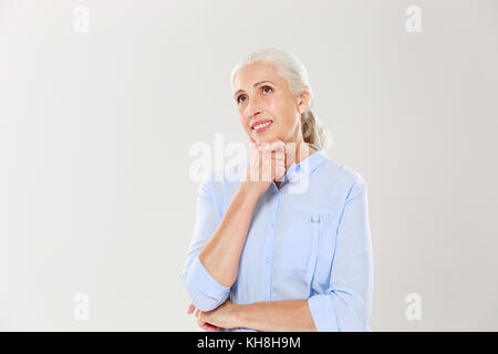 Portrait von Träumen heitere alte Dame, ihr Kinn berühren, abgesehen suchen, auf weißem Hintergrund Stockfoto