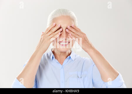 Ältere grauhaarige Frau, die ihre Augen mit beiden Händen, auf weißem Hintergrund Stockfoto