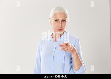 Portrait von verspielten ältere Frau mit dem Finger auf sie zeigend, auf weißem Hintergrund Stockfoto