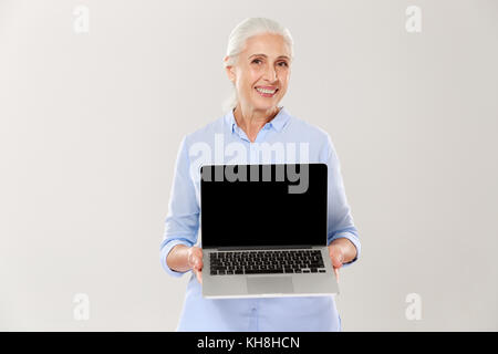 Wunderschöne reife grauhaarige Frau lächelnd und mit leerer Bildschirm des Laptop Computer isoliert Stockfoto