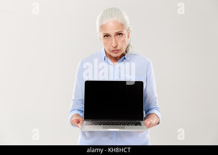 Zornig traurig reife Frau im blauen Hemd holding Laptop mit leerer Bildschirm islated über Weiß Stockfoto