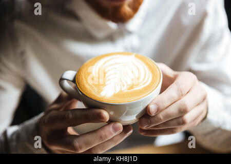7/8-Foto von Mann im weißen Hemd Holding heiße Tasse Kaffee Stockfoto