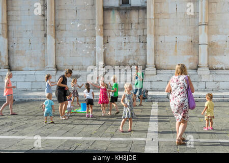 Kinder jagen Blasen vor der Kirche von San Michele in Foro, Piazza San Michele, Lucca, Toskana, Italien. Stockfoto