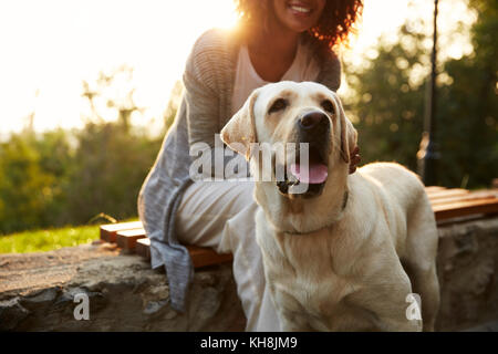 7/8 Schuß von jungen afrikanischen Dame tragen weiße Kostüm Wandern mit Hund im Park Stockfoto