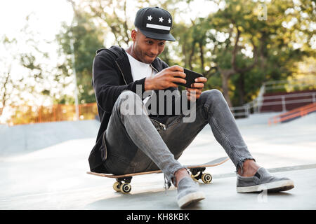 Porträt eines afrikanischen Kerl spielen auf Mobiltelefon während Rest in der städtischen Zone Stockfoto