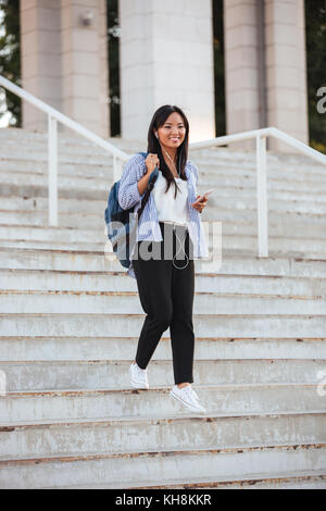 In voller Länge Porträt der jungen gerne asiatische Frau, wandern die Treppe hinunter, während Sie Musik hören, Außenpool Stockfoto