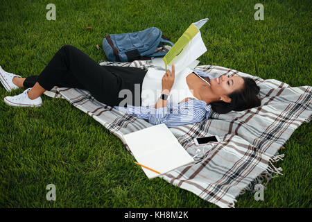 Junge freundliche asiatische Studentin Buch, Lesen, die auf dem Gras, outdoor Stockfoto