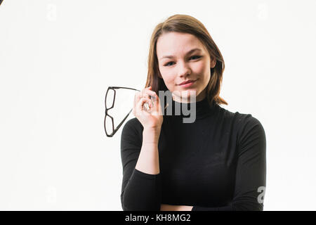 Intelligenz: Eine junge Braunhaarige kaukasischen Jugendmädchen trägt einen schwarzen rollkragen pullover und halten ein Paar schwarze Hornbrille Stockfoto