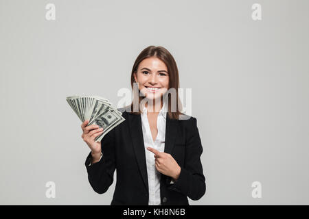 Porträt eines lächelnden hübsche Geschäftsfrau, die in der Klage holding Bündel geld Banknoten und Zeigefinger auf weißem Hintergrund Stockfoto