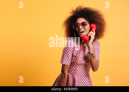 Schönen Lächeln afrikanische Frau im Kleid mit retro Telefon über gelben Hintergrund posiert Stockfoto