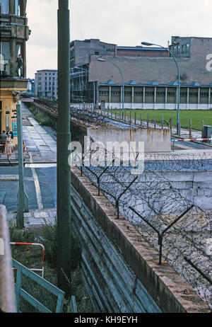 Blick über die Berliner Mauer aus dem Westen Deutschlands in den Osten Deutschland Suche im August 1965. Die Mauer ist in Stacheldraht und eine weibliche Touristische abgedeckt ist ein Foto mit einem Soldaten, die von einem Fenster im Obergeschoss in einem nahe gelegenen Gebäude. Stockfoto