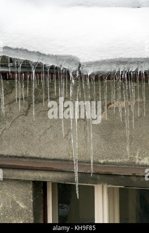 Eiszapfen hängen von einem schneebedeckten Dach. Frost mit eiszapfen an der Traufe des Hauses. gefährliche Eiszapfen hängen über der Straße in der Stadt. Stockfoto