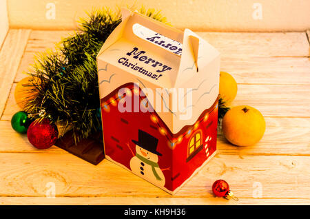 Rote und weiße Kasten mit einem Schneemann und einen Weihnachtsbaum. Zusammensetzung des neuen Jahres. Gelbe Stimmung. Obst und Spielzeug. Stockfoto