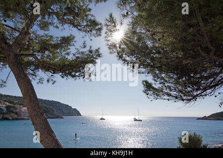 Bäume, Sonne, Boote und die Leute am Strand an einem sonnigen Tag am 30. Oktober 2017 in Sant Elm, Mallorca, Balearen, Spanien. Stockfoto