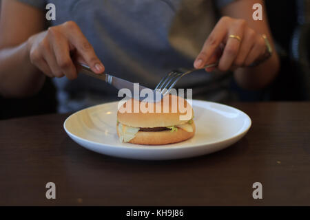 Frau bereiten schneiden Burger in zwei Hälften wählen Sie Fokus, halten schneiden Burger, Burger in zwei Hälften auf Tisch wenig Licht Stockfoto