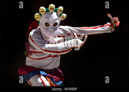 Tbetan Mönch in einem Anzug und einer Maske von einem Skelett mit weißen Totenköpfen führt einen heiligen Tanz der Tsam, Nahaufnahme, einem schwarzen Hintergrund. Stockfoto