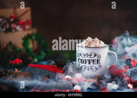 Heiße Schokolade mit Marshmallows in einem gemütlichen Emaille Tasse mit Dampf- und Weihnachtsdekorationen Stockfoto