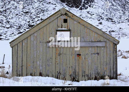 Alte abgeplatzte Holz- Rorbu - Fischen Hütte über schneebedeckte Boden - traditionelle Bootshaus mit Karte von der Küstenregion auf der Fassade-Schloss geschlossen schwenkbaren Doo Stockfoto