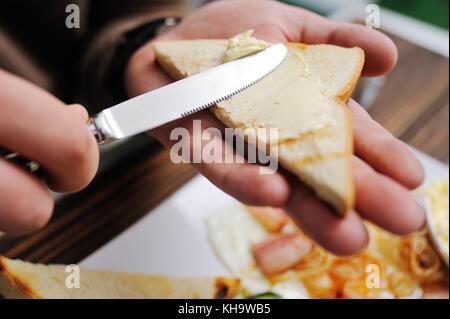 Hand mit einem Messer schmiert Butter auf Brot close-up auf einem Frühstück Hintergrund Stockfoto