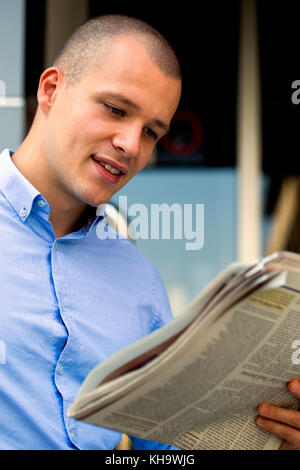 Portrait von schönen und positiven Geschäftsmann beim Stehen vor dem Bürogebäude und Zeitung lesen Stockfoto