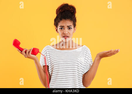 Junge afrikanische unzufrieden Unzufrieden Dame in legere Kleidung halten roten Hörer beim Stehen isoliert Stockfoto