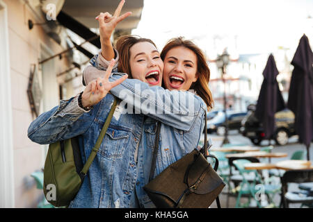 Foto von zwei hübsche Brünette weibliche Freunde Umarmen, Friedenszeichen, Kamera auf Stadt. Stockfoto