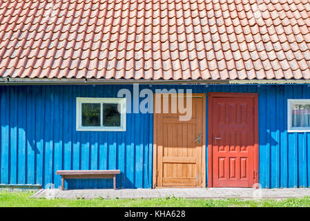 Haus der blauen Holzbohlen, rotem Dach, zwei bunte Türen und kleinen Fenstern Stockfoto