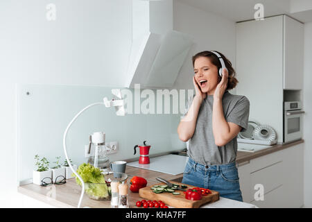 Porträt eines fröhliche Frau Musikhören mit Kopfhörern und Gesang beim Kochen in der Küche Stockfoto