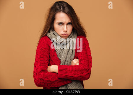 Portrait von umgekippt Einfrieren Frau in Rot in Form gestrickter Pullover mit gekreuzten Händen, von der Kamera suchen, auf beige Hintergrund isoliert Stockfoto