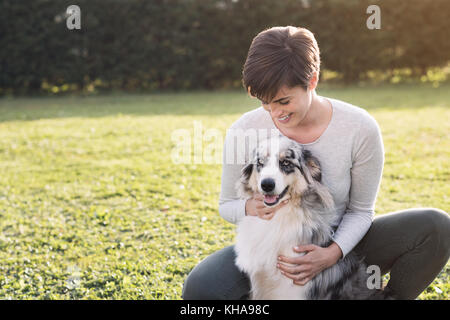 Schöne Frau und ihrem Hund zusammen in den Garten stellen an einem sonnigen Tag, Haustiere und Freizeit Konzept Stockfoto