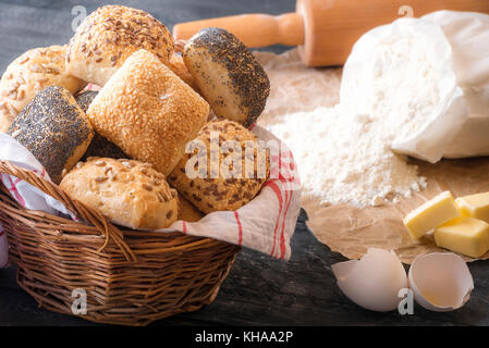 Backen Thema Bild mit einem Weidenkorb voll mit hausgemachten Brötchen, Mehl, Eierschale, Butter und einem Nudelholz umgeben, auf einem rustikalen Holzmöbeln Tabl Stockfoto