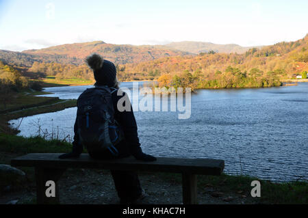 Frau Walker in bobble Hut auf Holzbank mit Blick auf rydal Wasser im Herbst im Nationalpark Lake District, Cumbria sitzen fiel, UK. Stockfoto