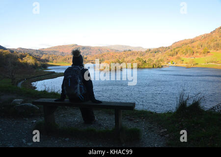 Frau Walker in bobble Hut auf Holzbank mit Blick auf rydal Wasser im Herbst im Nationalpark Lake District, Cumbria sitzen fiel, UK. Stockfoto