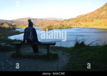 Frau Walker in bobble Hut auf Holzbank mit Blick auf rydal Wasser im Herbst im Nationalpark Lake District, Cumbria sitzen fiel, UK. Stockfoto