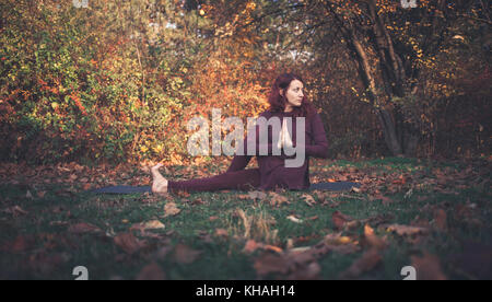 Mädchen auf einen Herbst Tag Üben Yoga im Freien, Ardha Matsyendrasana (halbe Herr der Fische, vakrasana oder die Hälfte der Wirbelsäule verdrehen), Arme vor Stockfoto