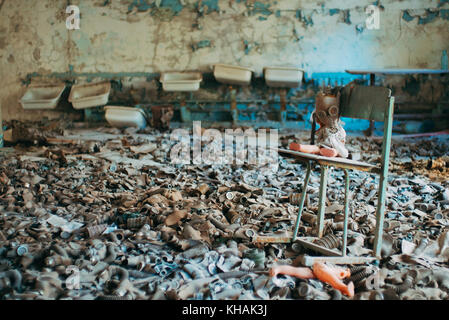 Ein Kind Puppe ist Aufgestützt auf einen Stuhl in einem Meer von Kinder- und Gasmasken Überbleibsel aus dem Kalten Krieg in einer verlassenen Schule in Pripyat, Tschernobyl Stockfoto