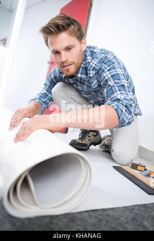 Junge männliche Heimwerker rolling Teppich auf dem Boden zu Hause Stockfoto