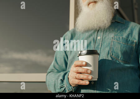 Schöner bärtiger alter Mann in lässiger Kleidung, der eine Tasse Kaffee hält Stockfoto
