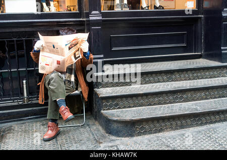 Ein Mann, der auf einem Klappstuhl sitzt und die Financial Times auf der Prince Street in SoHo, New York City liest Stockfoto