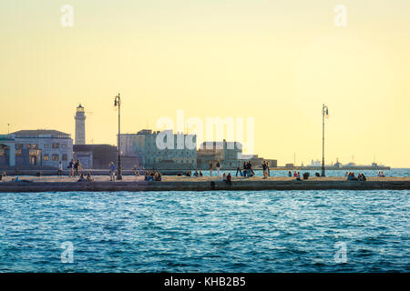 Hafen von Triest, Blick direkt nach Sonnenuntergang auf die Menschen, die entlang des riesigen Steinstegs Molo Audace im Hafen von Triest, Italien, spazieren. Stockfoto
