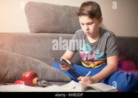 Jungen kaukasischen Jungen, der seine Hausaufgaben sitzen auf dem Bett mit Taschenrechner. Bildung Konzept. Stockfoto