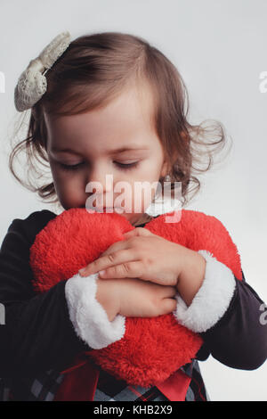 Süßes kleines Kind Mädchen Porträt halten roten Herzen Spielzeug auf weißem Hintergrund. happy holidays Konzept. Stockfoto