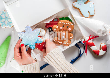 Die Vorbereitung auf Weihnachten, Verzierung traditionellen Lebkuchen mit bunten Zucker Glasur, das Mädchen faltet die Cookies in einem weißen Geschenkbox, mit Band Stockfoto