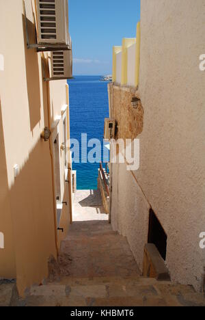 Ein schmaler Pfad hinunter zwischen Gebäude am Hafen von emborio auf der griechischen Insel Chalki. Stockfoto